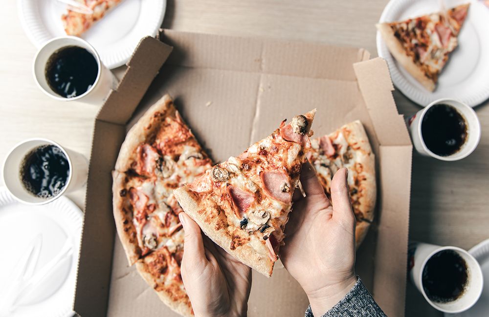 young-woman-holding-slices-of-hot-pizza-from-cardboard-box-at-table-top-view.jpg